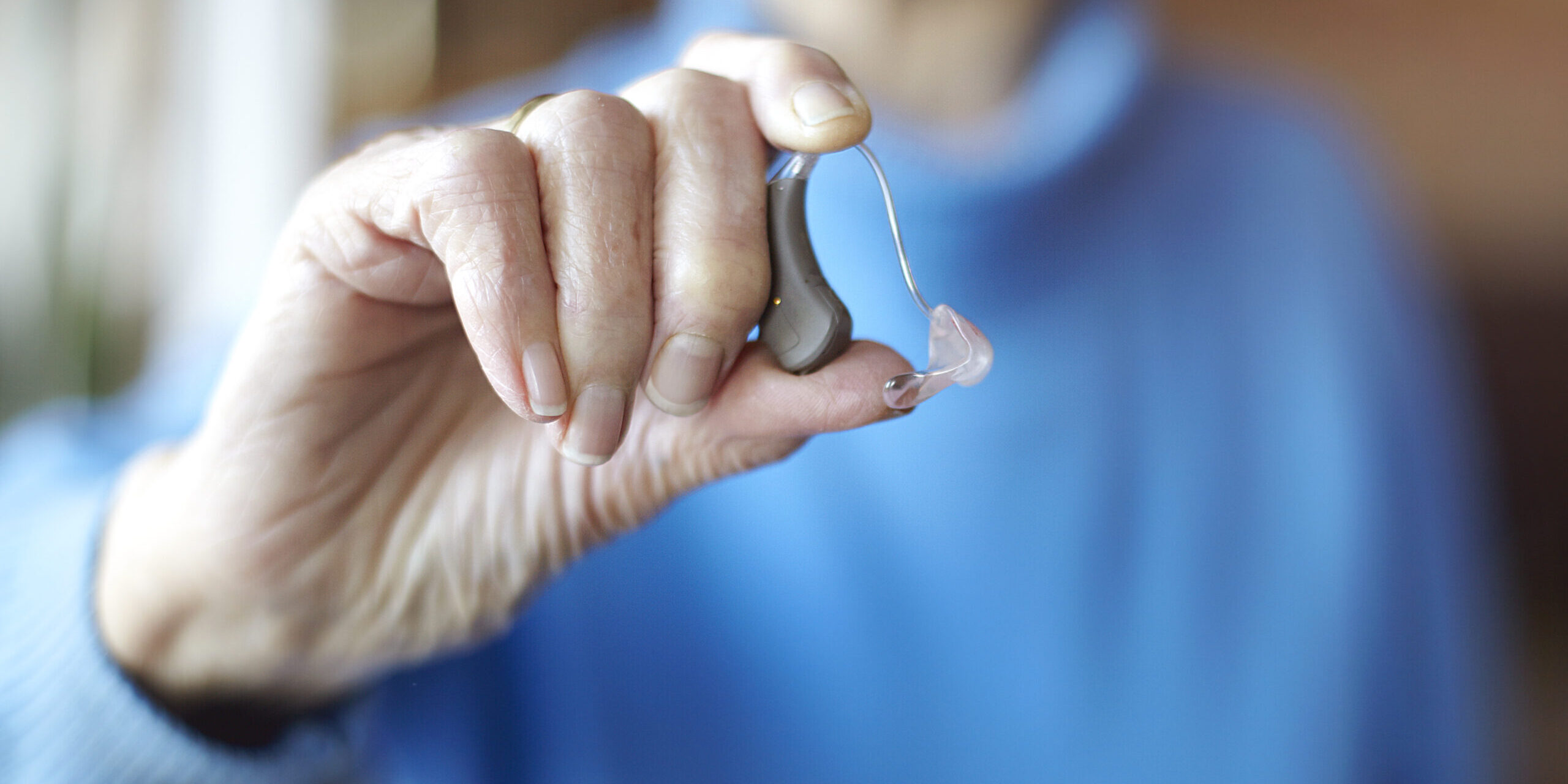 Senior woman holding hearing aid, close-up